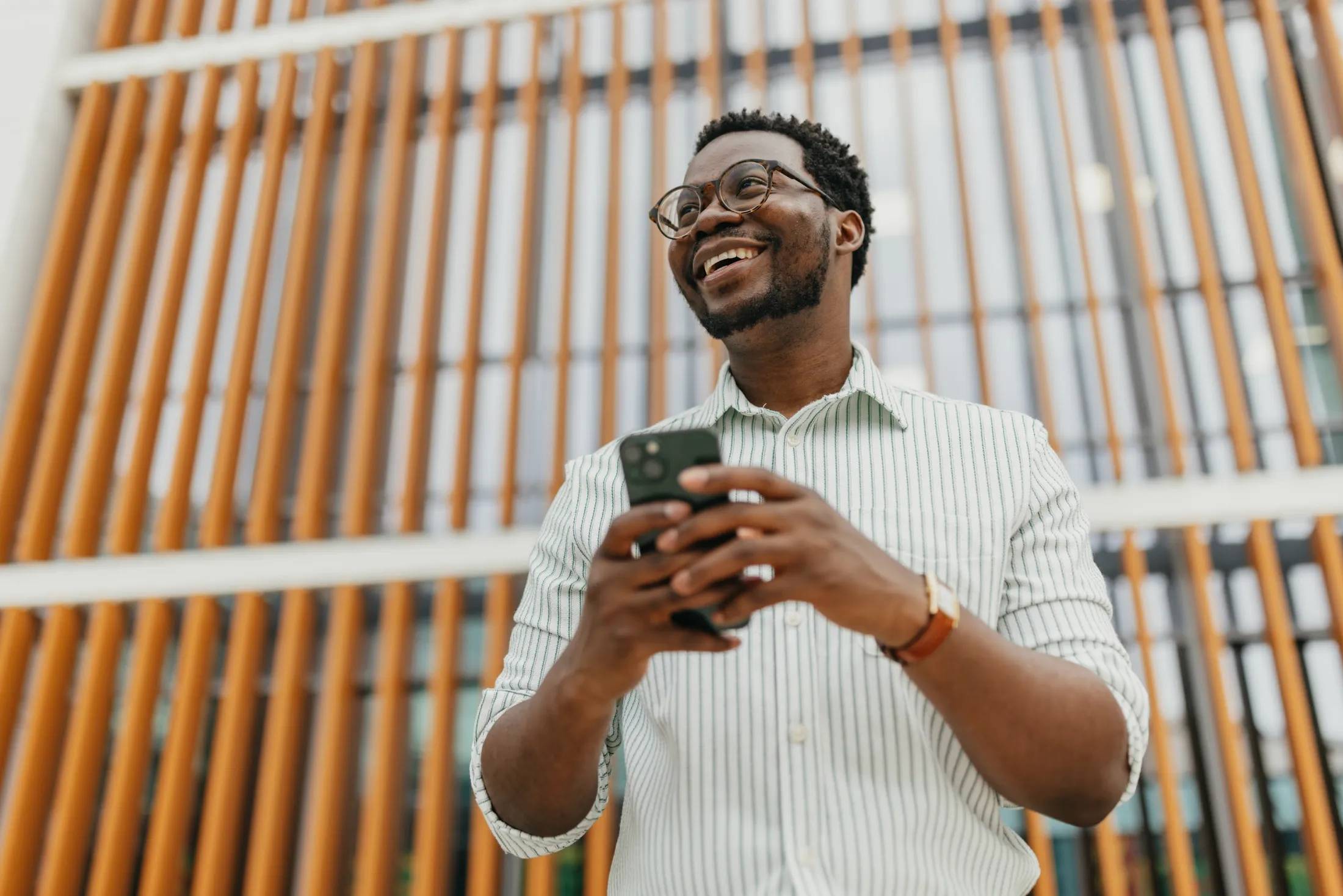 Confident young professional using smartphone outside modern office building.